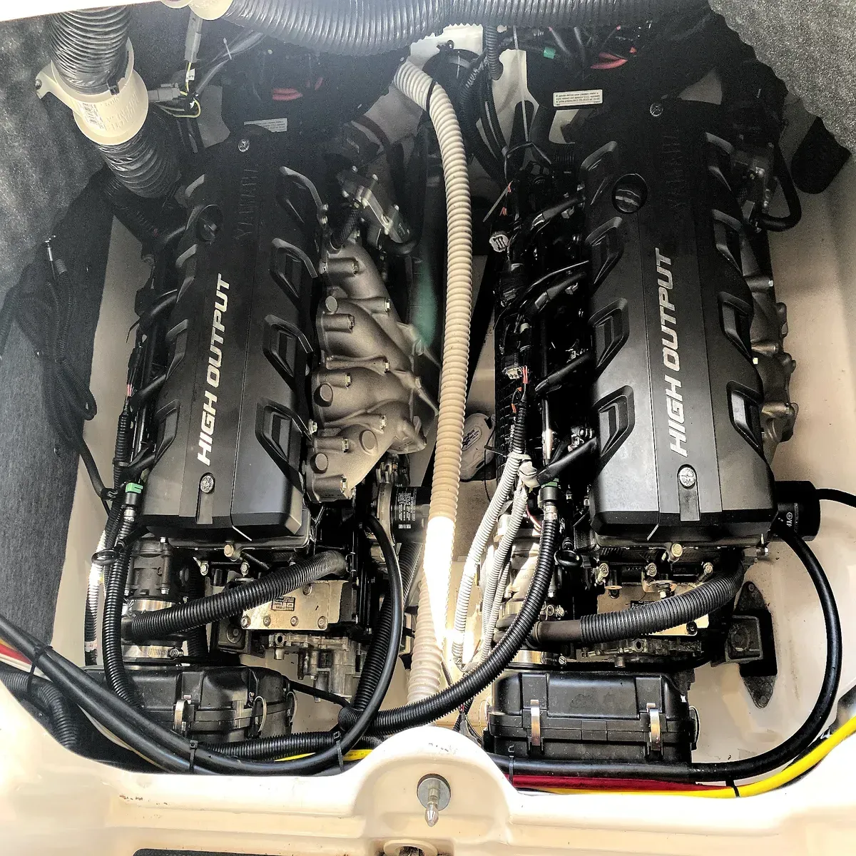 Twin black marine engines in an engine compartment, with hoses and wiring visible.