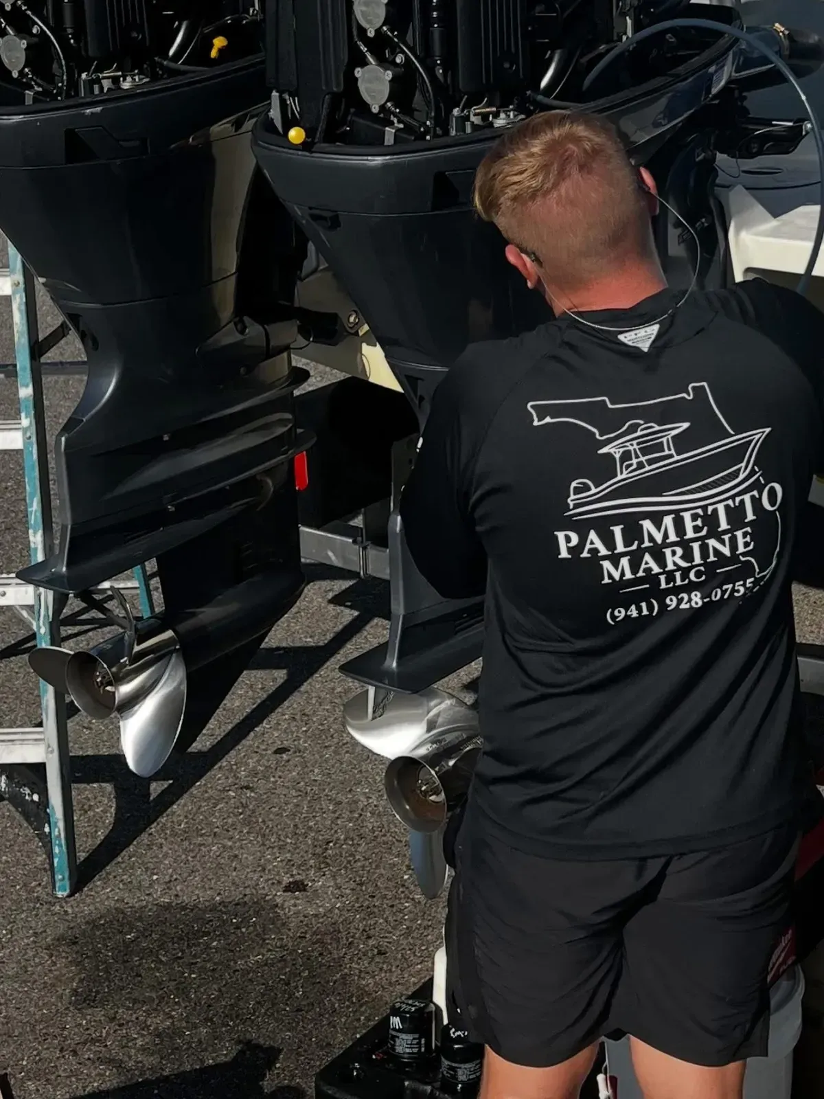 Man in black shirt inspecting boat motors on a dock, with Palmetto Marine logo visible on his back