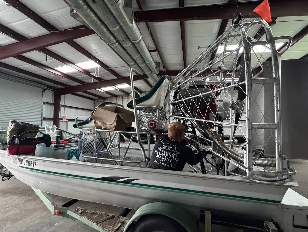 Person seated on a sailboat in a hangar, with a large metal rig and red flag overhead.