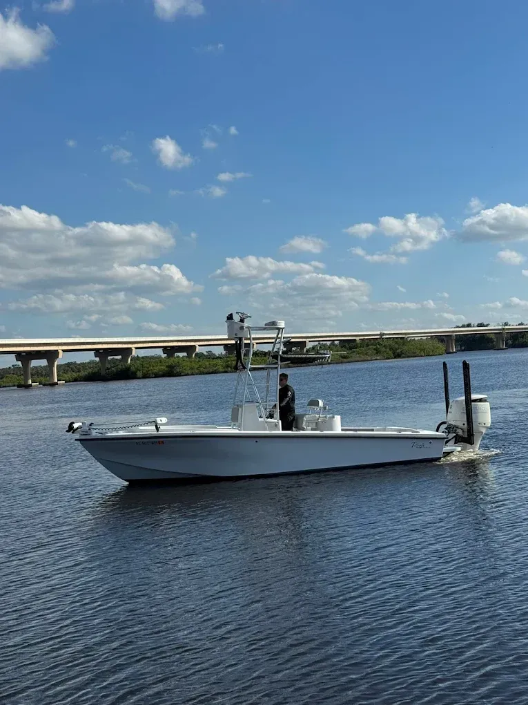 White motorboat on calm water under a blue sky with a bridge in the background