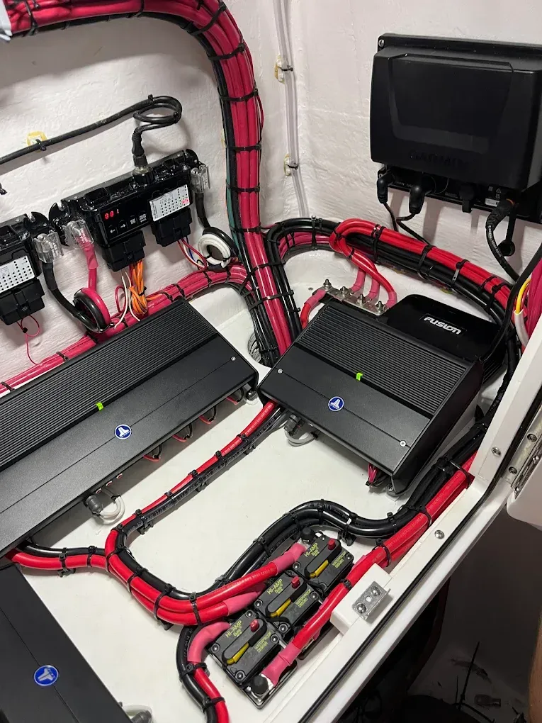 Red and black wiring in a car audio/electronics installation with two amplifiers and a screen mounted on the wall