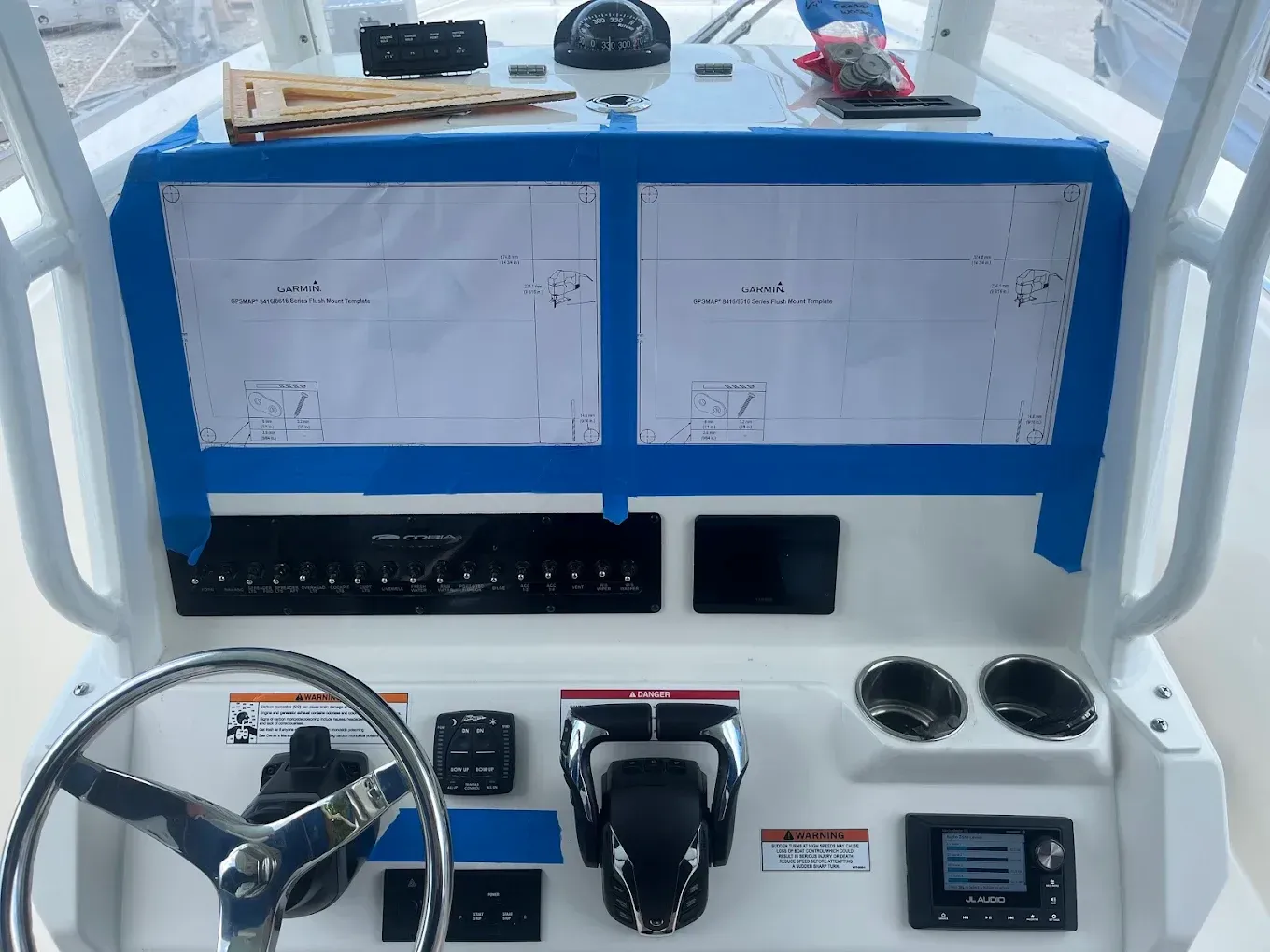 Blue boat helm with steering wheel, throttle, gauges, and two charts on the console.