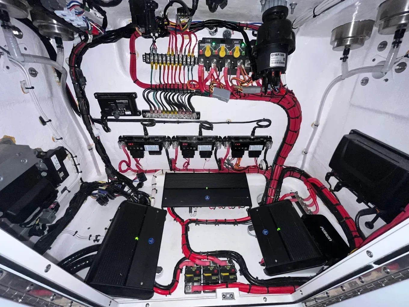 Interior of a car trunk with exposed wiring, fuse panels, and black audio/electrical components