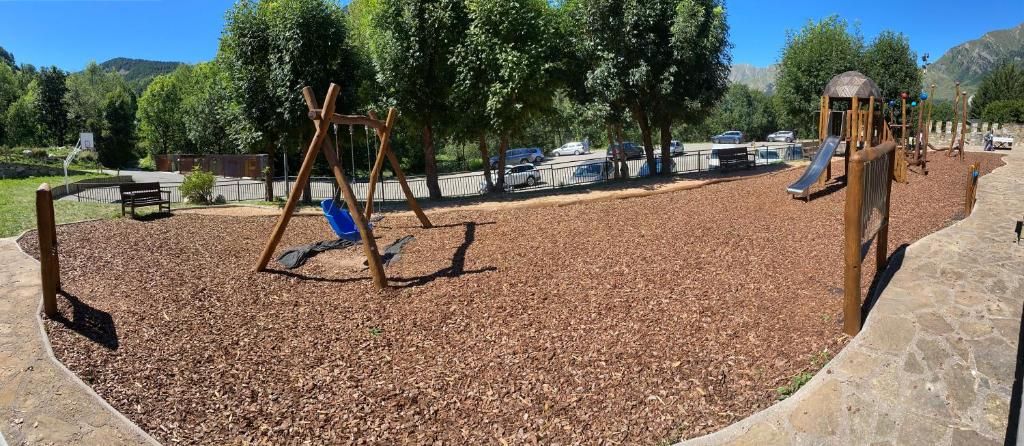 Parc infantil amb gronxadors, tobogan i estelles de fusta, situat en un parc amb arbres i muntanyes al fons.