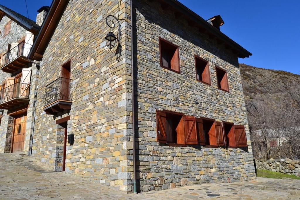 Casa de pedra amb persianes i porta de fusta, contra un turó i cel blau.