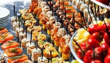 Buffet table with assorted colorful appetizers and skewers, including strawberries and fruit cups