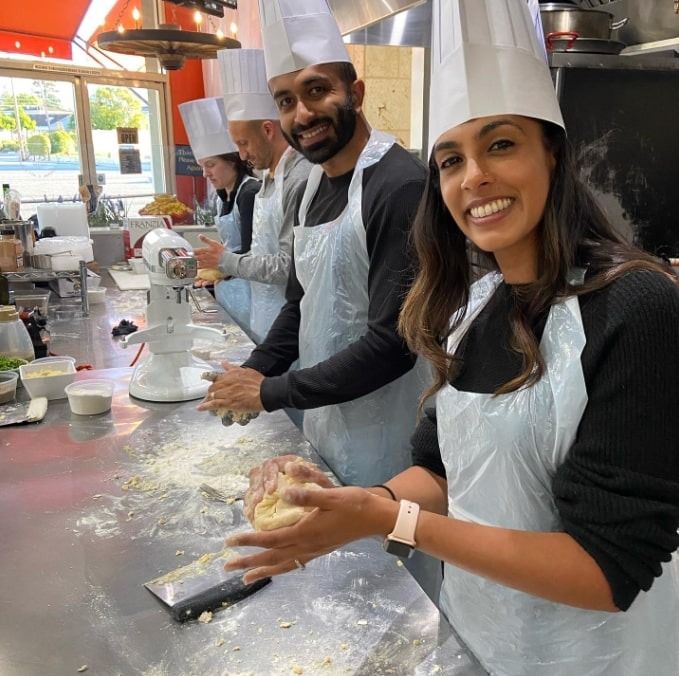 Two smiling chefs in aprons and hats knead dough in a flour-dusted kitchen