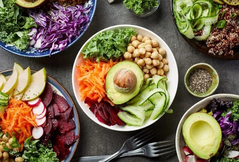 Assorted fresh salad bowls with avocado, vegetables, chickpeas, and greens on a dark table