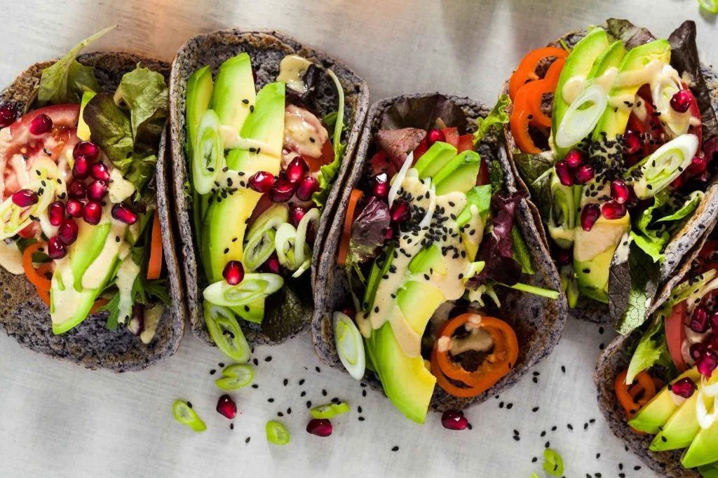 Avocado toast on dark bread, topped with pomegranate seeds, greens, and radish slices.