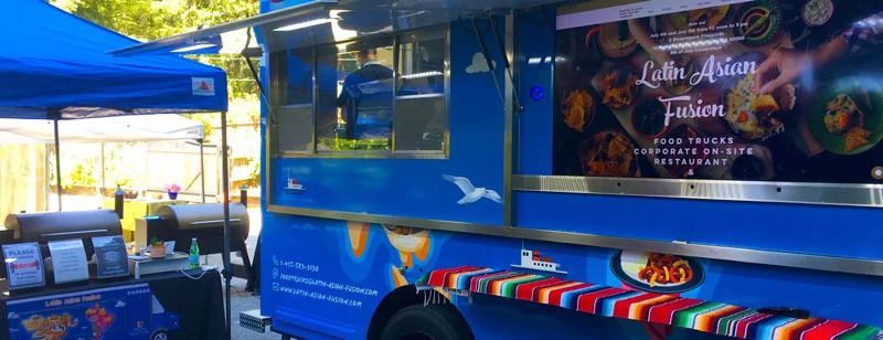 Blue food truck with colorful banners and a market stall under a canopy