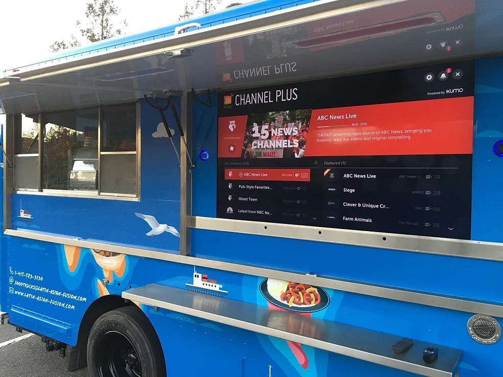 Blue food truck with a large digital menu screen on the side, parked outdoors.