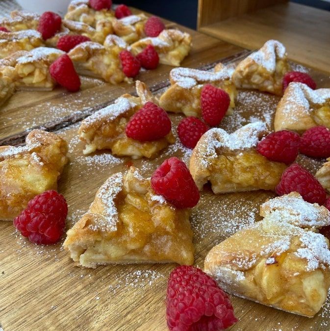 Pastries dusted with powdered sugar and topped with raspberries on a wooden board