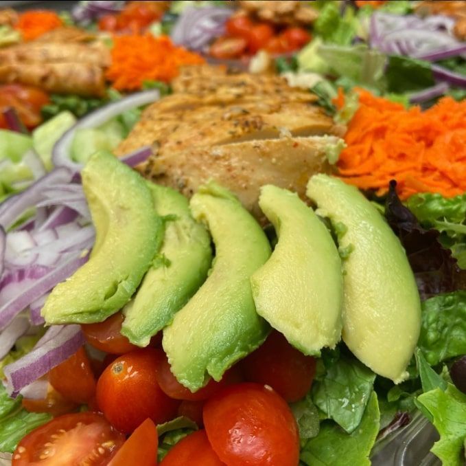 Avocado slices atop a colorful salad with cherry tomatoes, lettuce, onions, and seasoned chicken