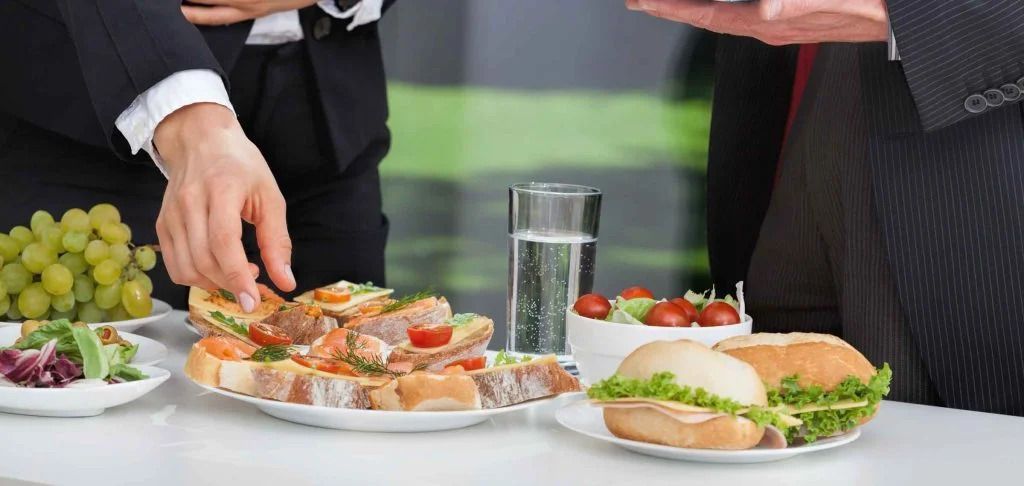 Hands serving appetizers and sandwiches at a buffet table with grapes and drinks