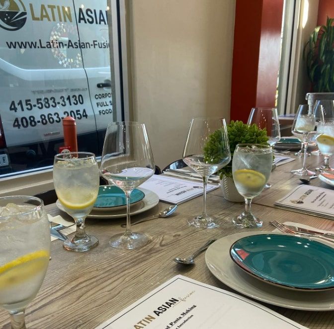 Restaurant table set with teal plates, water glasses, menus, and lemon drinks beside a window