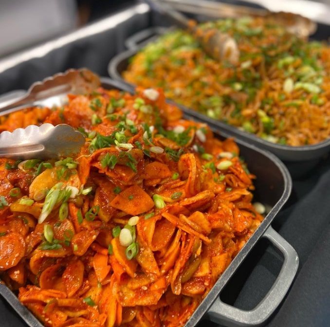 Trays of spicy stir-fried vegetables or meat topped with chopped green onions at a buffet
