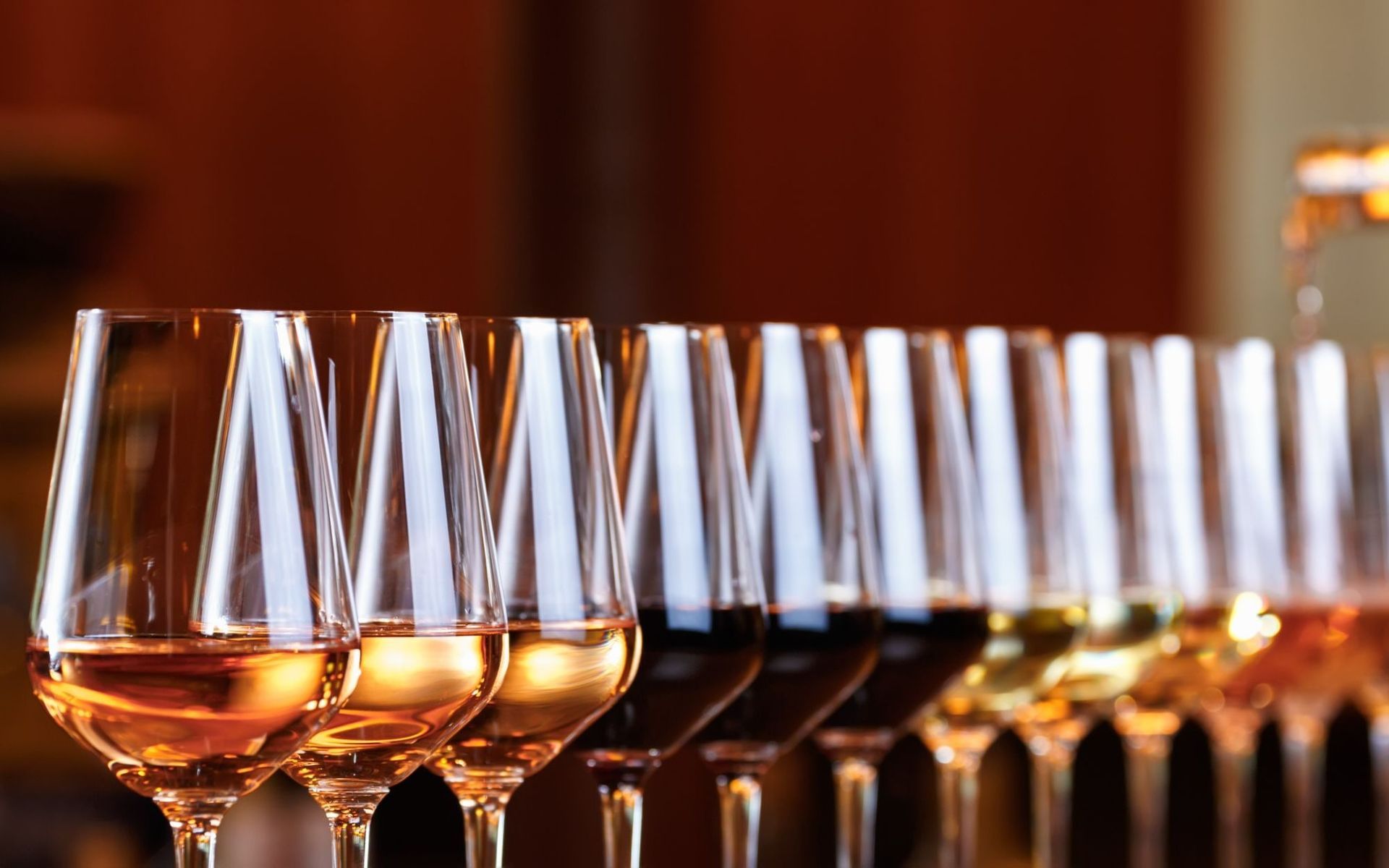 Rows of clear wine glasses filled with rosé on a table, with a warm blurred background