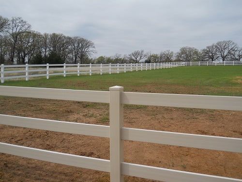 A white fence surrounds a grassy field with trees in the background