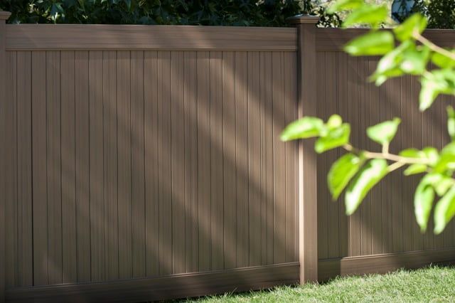 A brown wooden fence is surrounded by green grass and trees.
