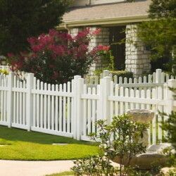 A white picket fence surrounds a lush green yard in front of a house.