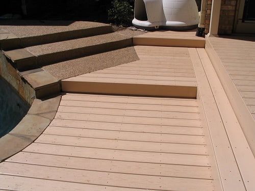 A wooden deck with stairs and a pool in the background
