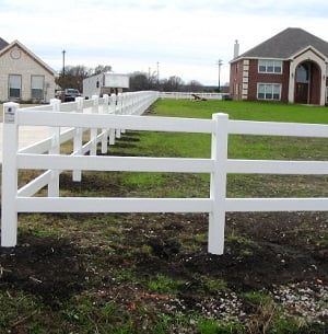 A white fence surrounds a lush green field in front of a house.