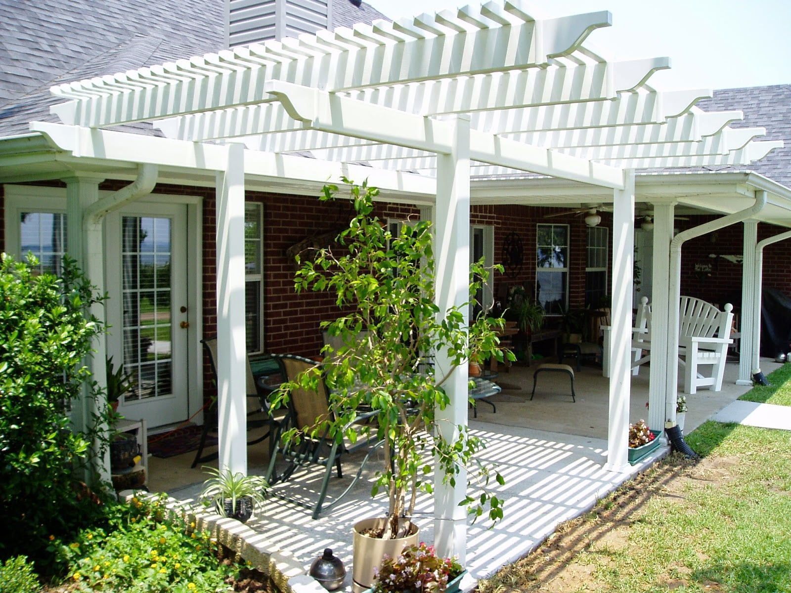 A white pergola over a patio with a brick house in the background