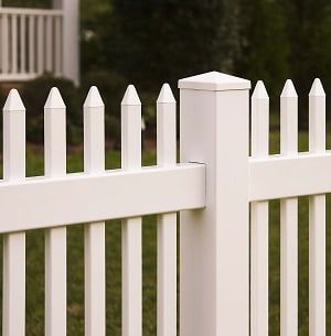 A white picket fence is sitting in the grass in front of a house.