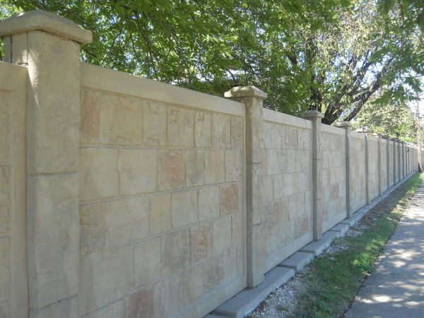 A stone wall along a sidewalk with trees in the background