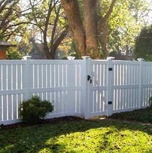 A white vinyl fence with a gate in the middle of a lush green yard.