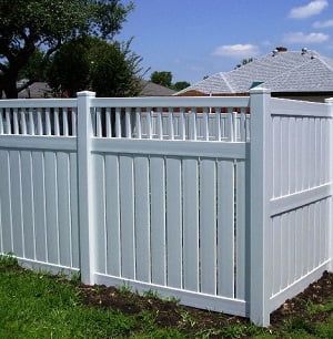 A white vinyl fence is sitting in the grass in front of a house.