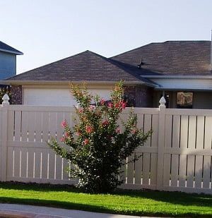 A white fence with a bush in front of it and a house in the background.