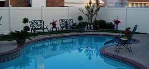 A large swimming pool surrounded by chairs and a white fence.