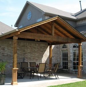 A wooden covered patio with a table and chairs under a roof.