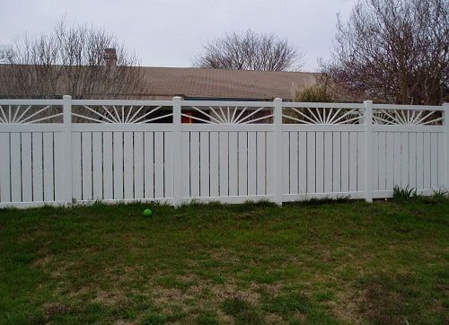 A white fence surrounds a lush green yard in front of a house.