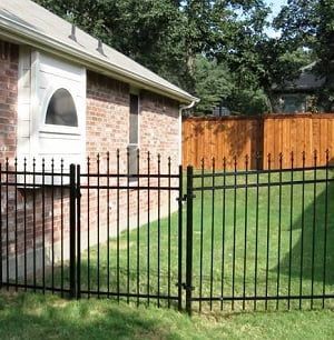 A brick house with a metal fence and a wooden fence in front of it.