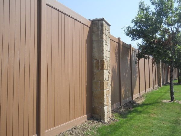 A wooden fence surrounds a stone wall in a yard.