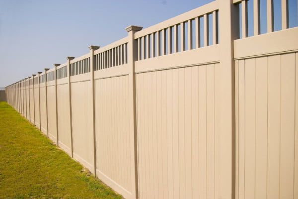 A long tan vinyl fence surrounds a lush green field.