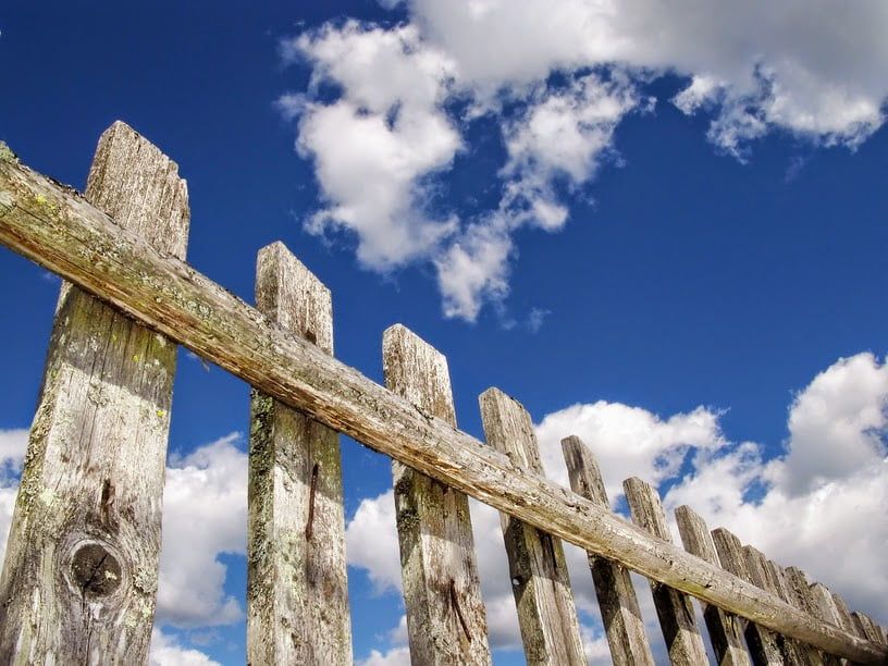 A wooden fence against a blue sky with clouds