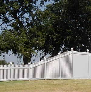 A white picket fence surrounds a grassy field with trees in the background.