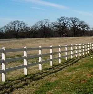 A white fence surrounds a grassy field with trees in the background.