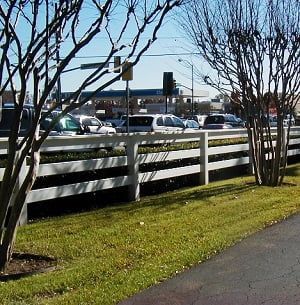 A white fence surrounds a grassy area with cars parked behind it