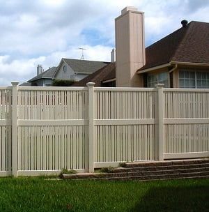 A white fence surrounds a lush green yard in front of a house.
