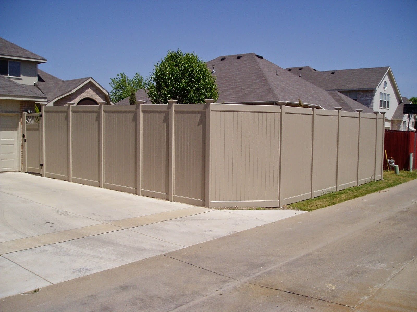 A tan fence surrounds a driveway in front of a house