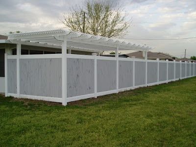 A white fence with a pergola attached to it in front of a house.