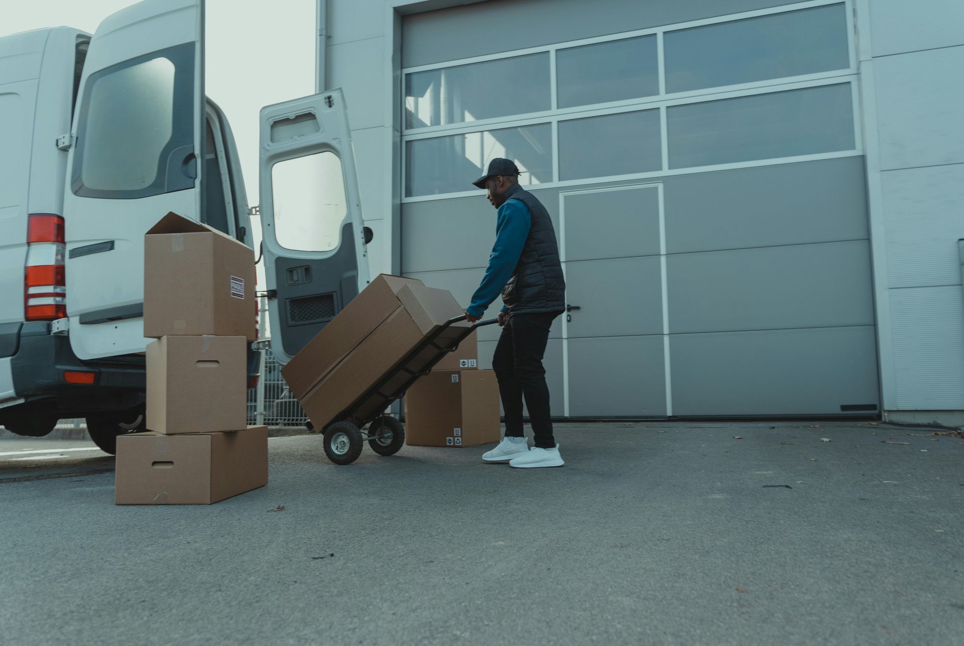 A man is pushing a cart with boxes in front of a van.