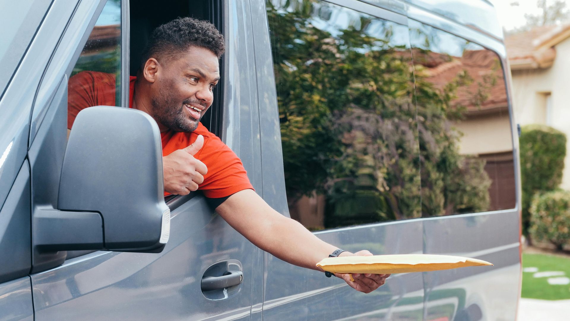 A delivery man is giving a thumbs up while holding an envelope.