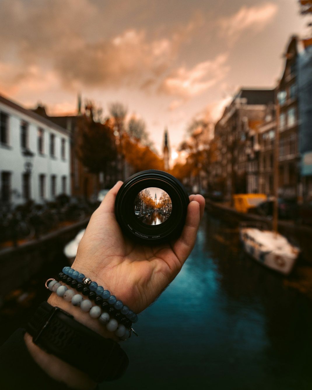 A person is holding a camera lens over a river.
