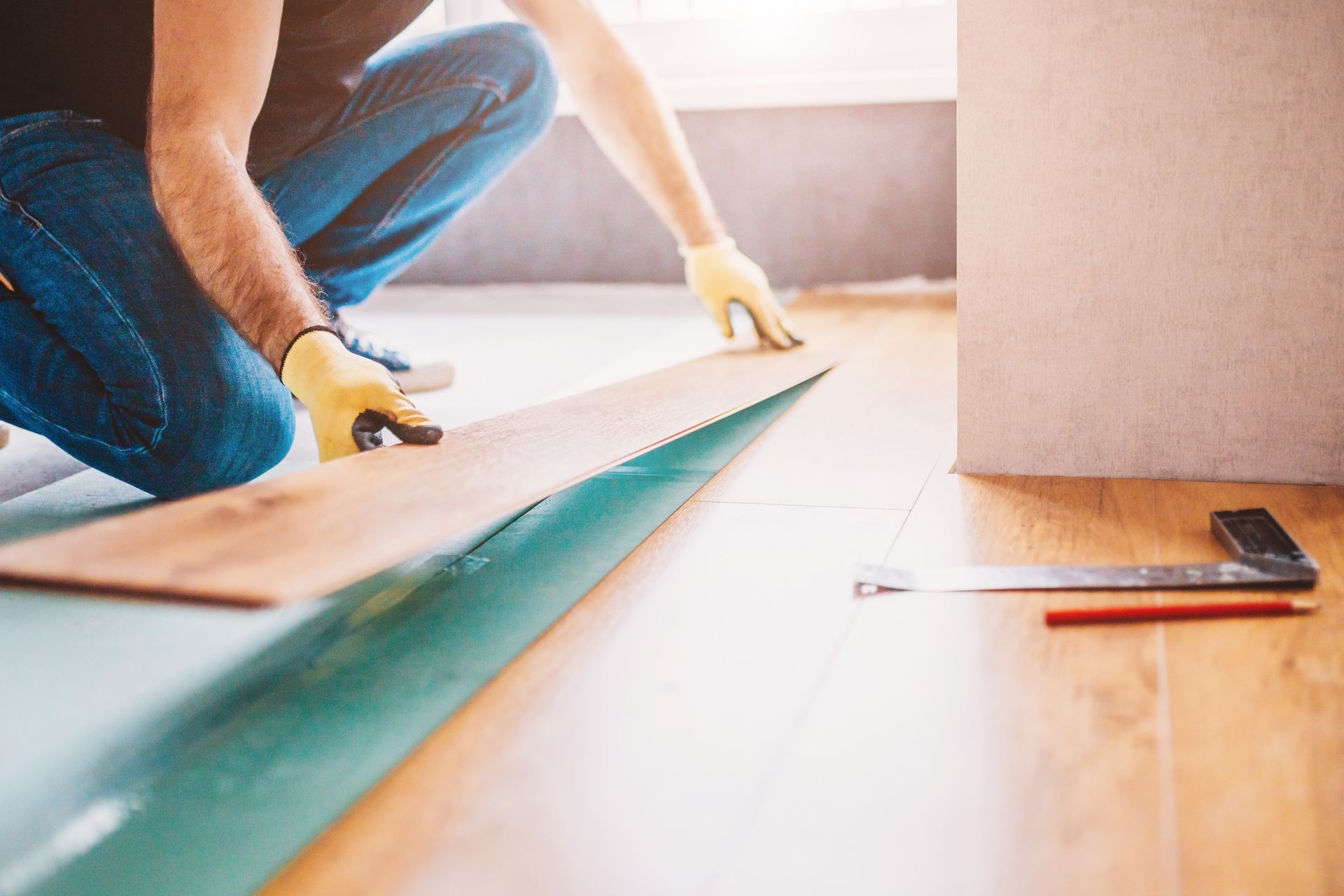 Person installing wood flooring, kneeling and working with tools and materials.