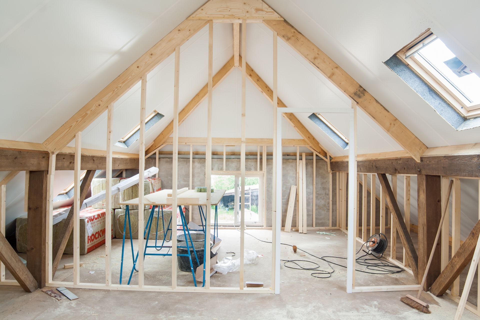 Interior of a room under construction with exposed wooden beams, studs, and skylights.